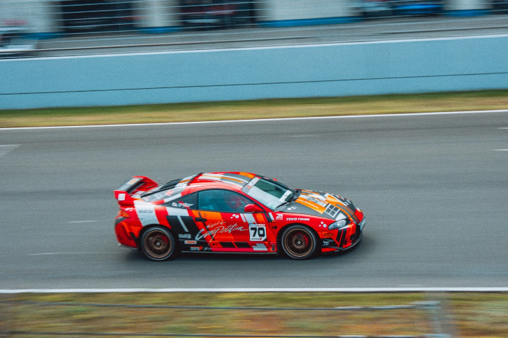 Orange-and-red Mitsubishi Eclipse speeding past the pit wall