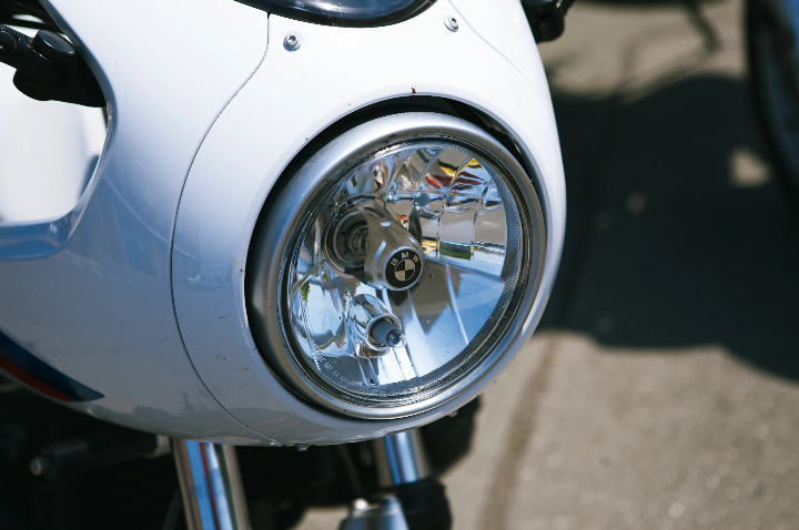 Close-up of a round chrome motorcycle headlight and white front fairing in bright sunlight