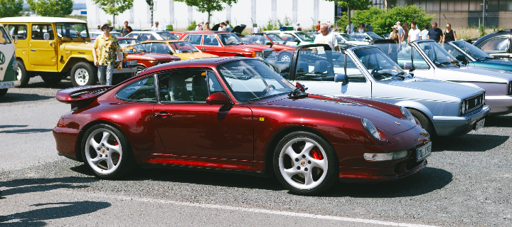 Red Porsche 911 parked among other classic cars at an outdoor vehicle exhibition in Kulmbach