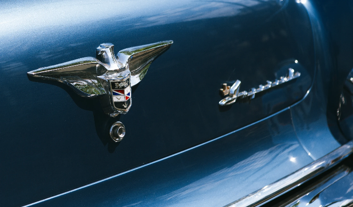 Chrome winged badge and script on the blue body panel of a vintage car