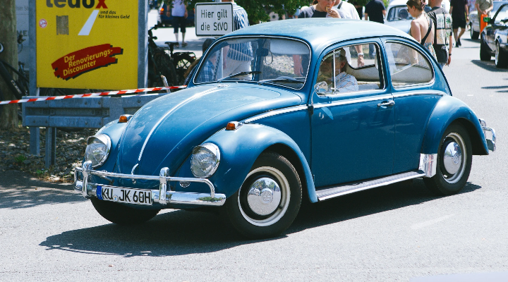 Blue classic Volkswagen Beetle with chrome bumpers and whitewall-style wheels, photographed from the front side