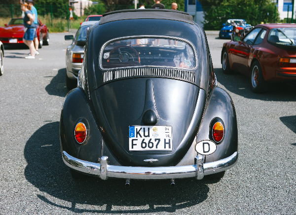 Rear view of a dark classic Volkswagen Beetle with oval rear window, chrome bumper and German registration plate
