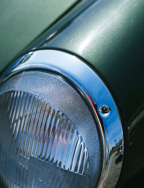 Extreme close-up of a vintage car headlight with ribbed glass lens, chrome surround and green metallic bodywork