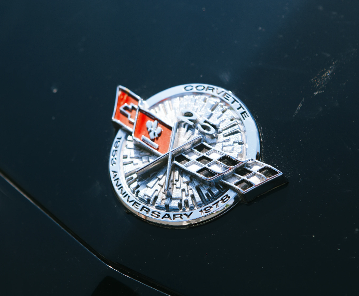 Close-up of a Chevrolet Corvette 25th Anniversary emblem with crossed flags on dark bodywork